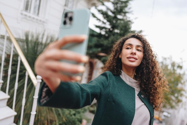 通りで写真を撮る巻き毛を持つ若いブルネットの女性