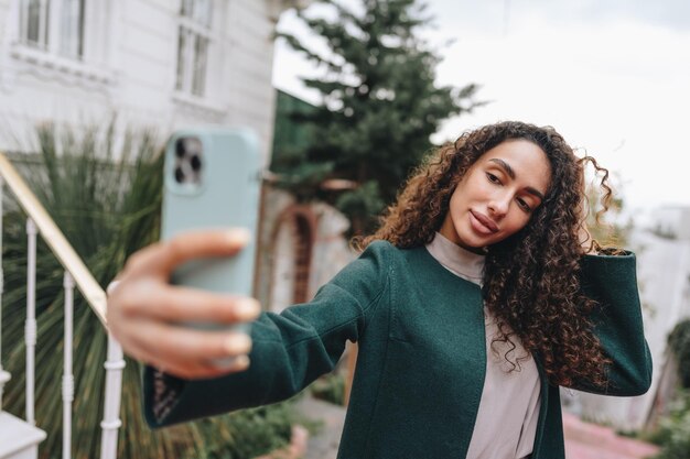 通りで写真を撮る巻き毛を持つ若いブルネットの女性