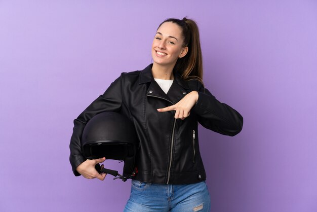 Young brunette woman with a motorcycle helmet over isolated purple wall and pointing it