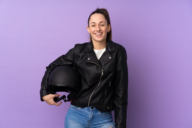 Young brunette woman with a motorcycle helmet over isolated purple wall with surprise and shocked facial expression