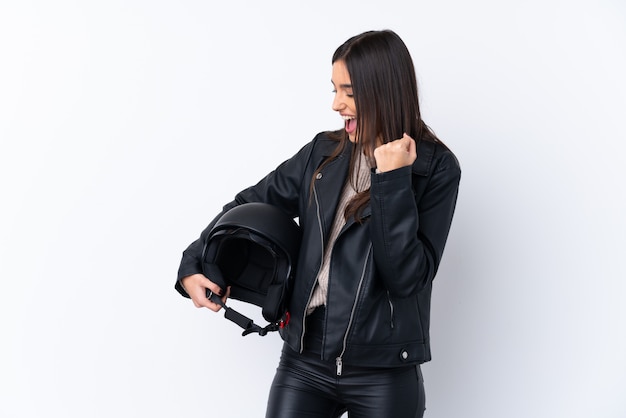 Young brunette woman with a motorcycle helmet over isolated white wall celebrating a victory