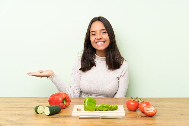 Young brunette woman with vegetables holding copyspace imaginary on the palm