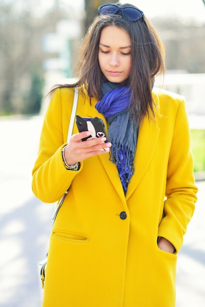 Young brunette woman in a yellow coat, reads on the phone.