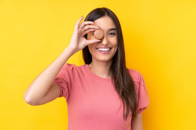 Young brunette woman over yellow holding colorful macarons