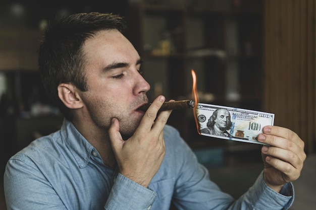 Young brutal businessman lighting cigar with 100 dollar bill as
a symbol of wealth and success the concept of wealth and
extravagance