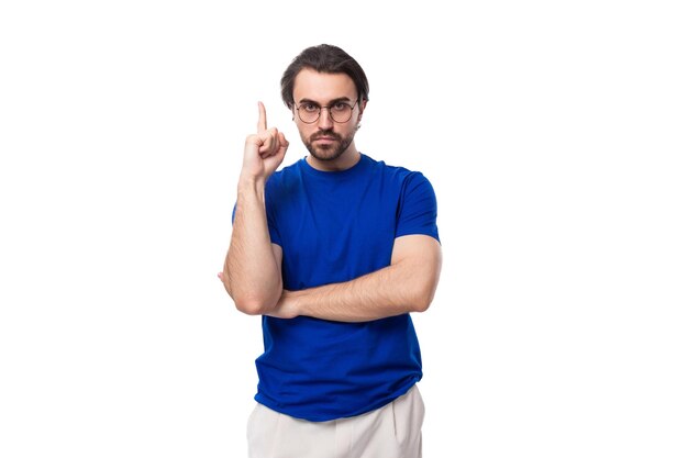 Молодой брутальный европейский брюнет с бородой, одетый в синюю футболку, жестикулирует своим
