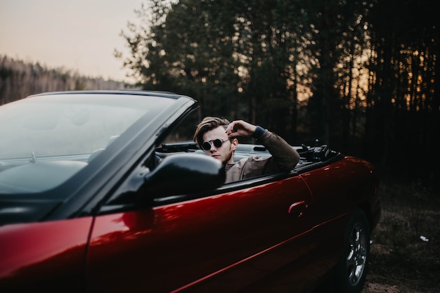 young brutal man in sunglasses sits in a luxury convertible car