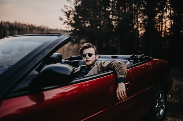 young brutal man in sunglasses sits in a luxury convertible car
