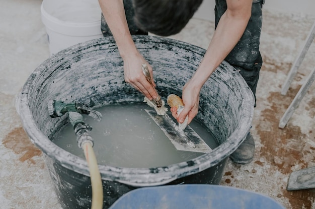A young builder washes spatulas in a basin