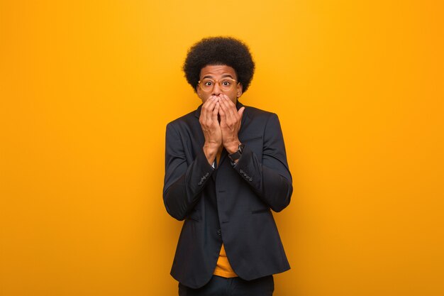 Young business african american man over an orange wall very sca and afraid hidden