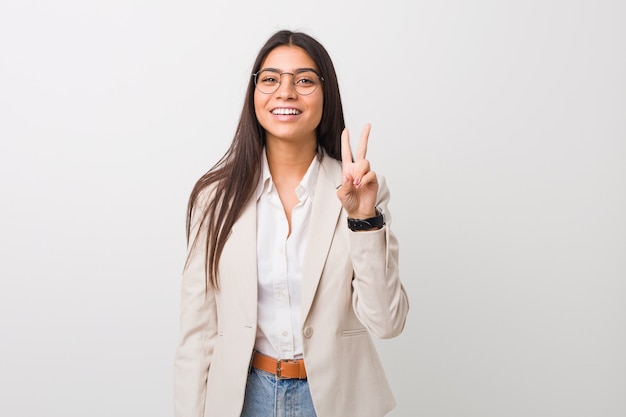 Young business arab woman isolated against a white wall showing victory sign and smiling broadly.