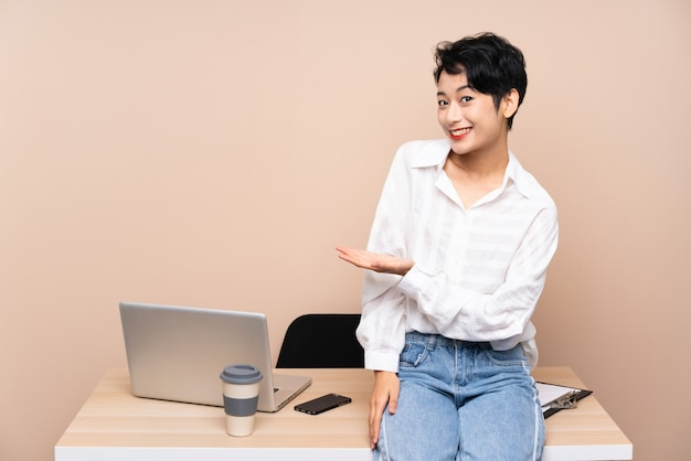 Young business Asian girl in her workplace extending hands to the side for inviting to come