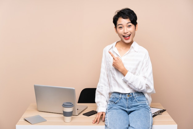 Young business Asian girl in her workplace pointing finger to the side