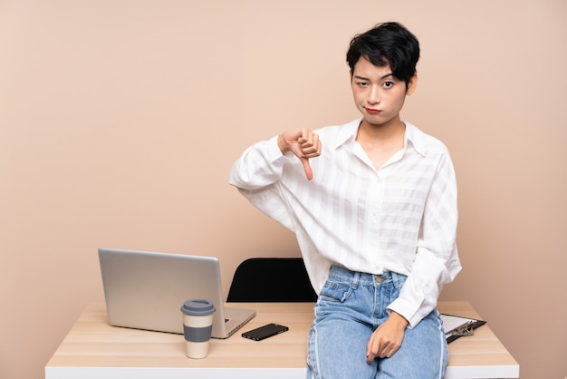 Young business Asian girl in her workplace showing thumb down sign