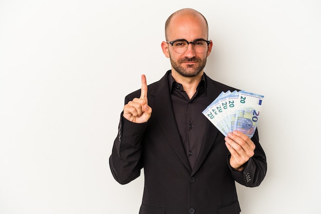 손가락으로 1번을 보여주는 흰색 배경에 격리된 지폐를 들고 있는 젊은 비즈니스 대머리 남자.