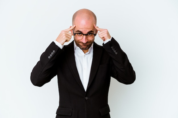 Young business bald man isolated on blue wall focused on a task, keeping forefingers pointing head