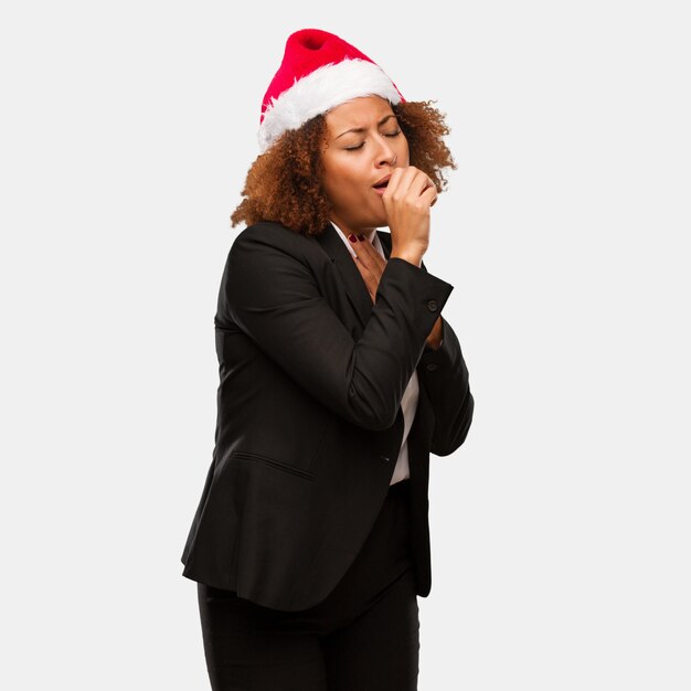 Young business black woman wearing a chirstmas santa hat coughing, sick due a virus or infection