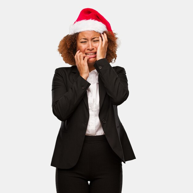 Young business black woman wearing a chirstmas santa hat desperate and sad