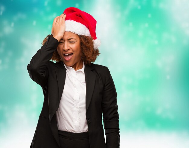 Young business black woman wearing a chirstmas santa hat forgetful, realize something