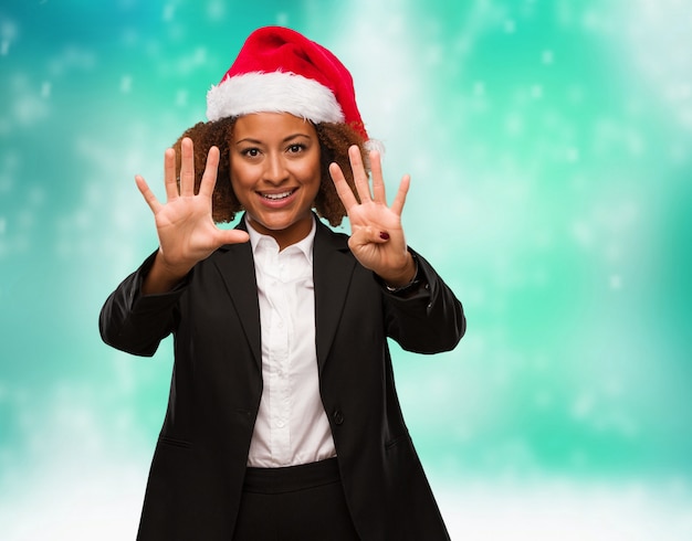 Young business black woman wearing a chirstmas santa hat showing number nine