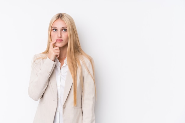 Young business blonde woman on white wall looking sideways with doubtful and skeptical expression.