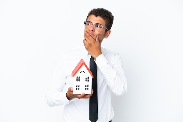 Young business Brazilian man holding a house toy isolated on white background having doubts