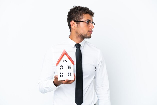 Young business Brazilian man holding a house toy isolated on white background looking to the side