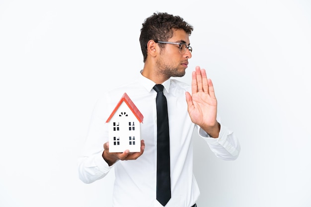 Young business Brazilian man holding a house toy isolated on white background making stop gesture and disappointed
