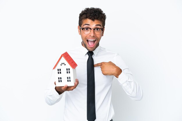 Young business Brazilian man holding a house toy isolated on white background with surprise facial expression