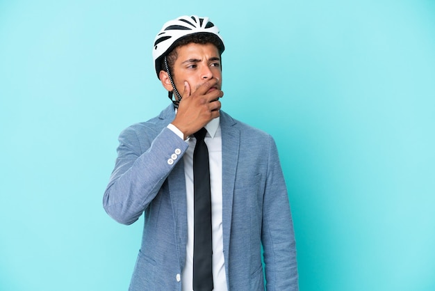 Young business Brazilian man with bike helmet isolated on blue background having doubts and with confuse face expression