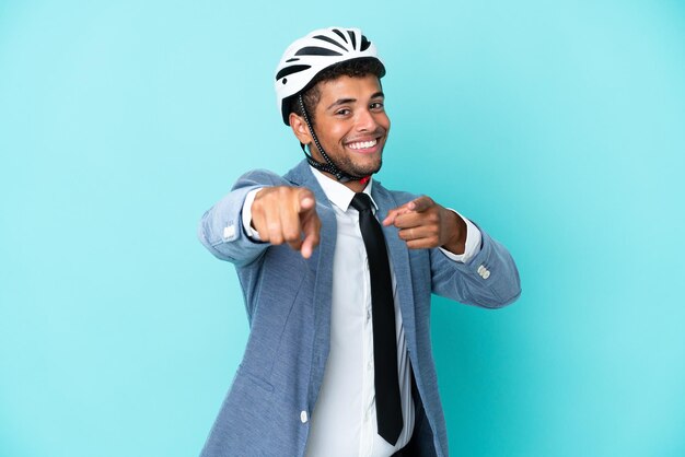 Young business Brazilian man with bike helmet isolated on blue background points finger at you while smiling