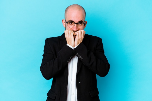 Young business caucasian bald man isolated on blue background biting fingernails, nervous and very anxious.