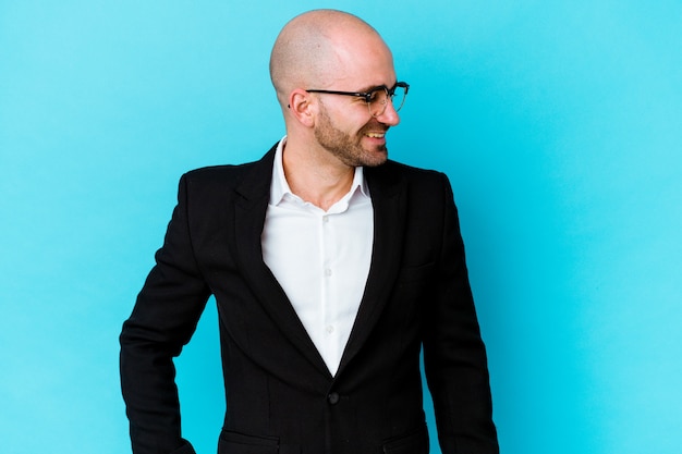 Photo young business caucasian bald man isolated on blue background laughs and closes eyes, feels relaxed and happy.