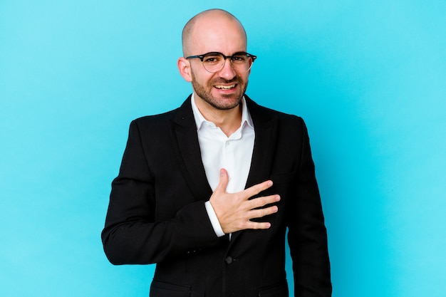 Young business caucasian bald man isolated on blue background laughs out loudly keeping hand on chest.