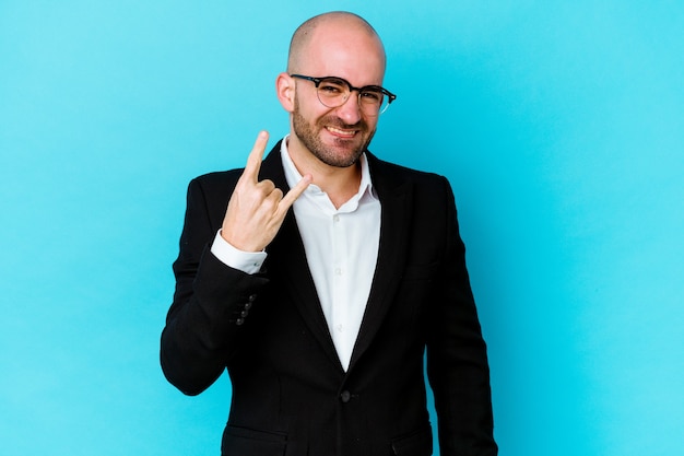 Young business caucasian bald man isolated on blue background showing rock gesture with fingers