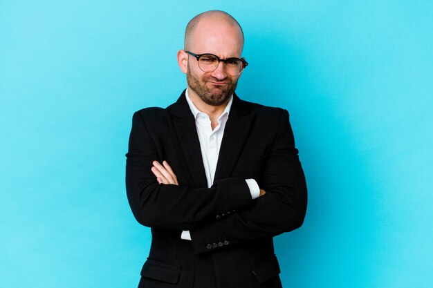 Young business caucasian bald man isolated on blue wall blows cheeks, has tired expression. Facial expression concept.