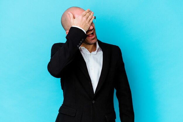 Young business caucasian bald man isolated on blue wall laughs joyfully keeping hands on head. Happiness concept.