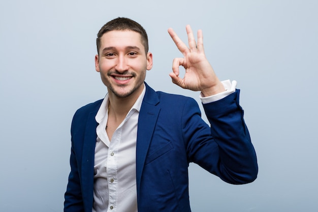 Young business caucasian man cheerful and confident showing ok gesture.