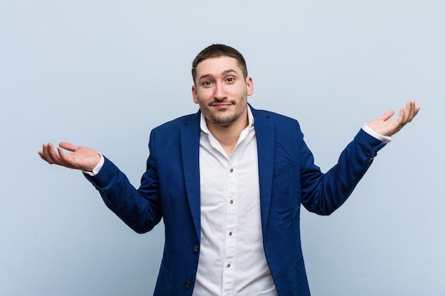 Young business caucasian man doubting and shrugging him shoulders in questioning gesture.