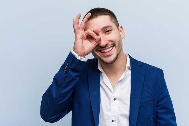 Young business caucasian man excited keeping ok gesture on eye.