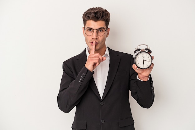 Young business caucasian man holding alarm clock isolated on white background keeping a secret or asking for silence.