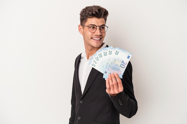 Young business caucasian man holding banknotes isolated on white background looks aside smiling, cheerful and pleasant