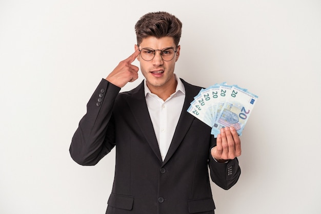 Young business caucasian man holding banknotes isolated on white background showing a disappointment gesture with forefinger.