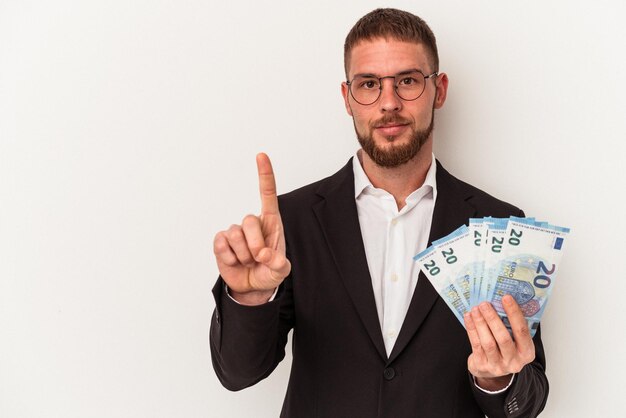 Young business caucasian man holding banknotes isolated on white background showing number one with finger.