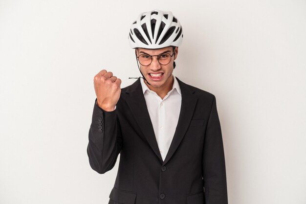 カメラに拳、攻撃的な表情を示す白い背景で隔離の自転車のヘルメットを保持している若いビジネス白人男性。