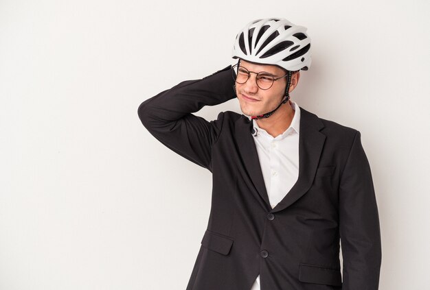 Молодой деловой кавказский человек, держащий велосипедный шлем, изолированный на белом фоне, касаясь затылка, думая и делая выбор.