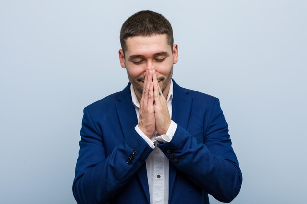 Young business caucasian man holding hands in pray near mouth, feels confident.