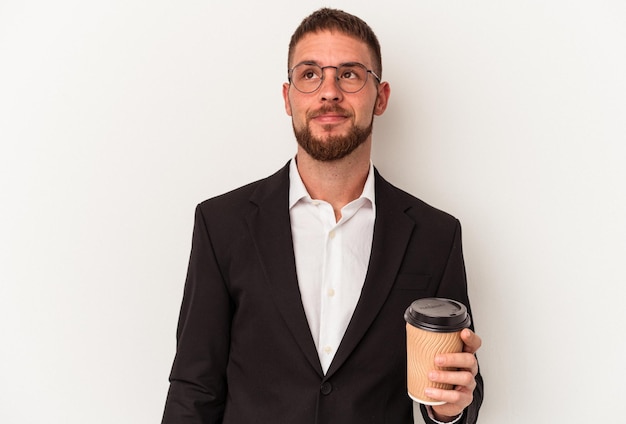 Young business caucasian man holding take away coffee isolated on white background dreaming of achieving goals and purposes