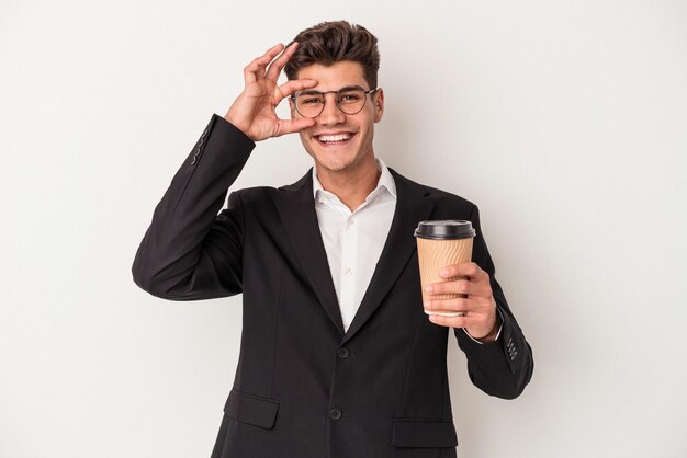 Young business caucasian man holding take away coffee isolated on white background excited keeping ok gesture on eye.