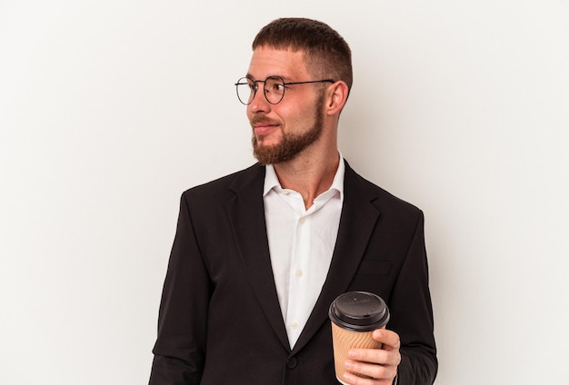 Young business caucasian man holding take away coffee isolated on white background looks aside smiling, cheerful and pleasant.